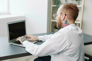 homme fauteuil roulant homme d'affaire avec tatouages dans le Bureau travaux à une portable en ligne, affaires processus de le dos, copie espace, l'intégration dans société, le concept de travail une la personne avec handicapées photo