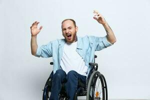 une homme dans une fauteuil roulant regards à le caméra colère et agression, avec tatouages sur le sien bras est assis sur une gris studio arrière-plan, santé concept homme avec handicapées photo