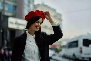 une sourire femme avec affaires les dents des promenades dans le ville contre le toile de fond de Bureau bâtiments, élégant à la mode vêtements et se maquiller, printemps marcher, Voyage. photo