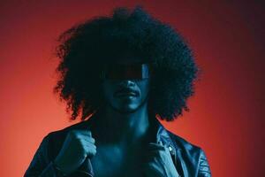 portrait de mode homme avec frisé cheveux sur rouge Contexte avec élégant lunettes, multiculturel, coloré lumière, noir cuir veste s'orienter, moderne concept. photo