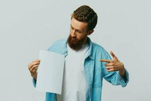 portrait de un adulte Masculin sur une gris Contexte avec une blanc feuille de papier dans le sien mains pour votre conception et texte, mise en page, copie espace, espace pour texte, doigt montrer du doigt photo