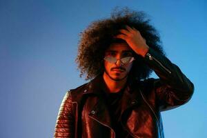 portrait de une élégant homme avec frisé cheveux sur une bleu Contexte multinational, coloré lumière, branché lunettes, moderne concept. photo