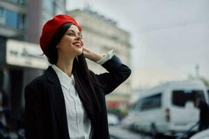 une sourire femme avec affaires les dents des promenades dans le ville contre le toile de fond de Bureau bâtiments, élégant à la mode vêtements et se maquiller, printemps marcher, Voyage. photo