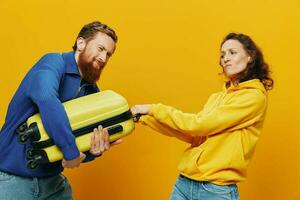 femme et homme souriant, les valises dans main avec Jaune et rouge valise souriant joyeusement et courbé, Jaune arrière-plan, Aller sur une voyage, famille vacances voyage, jeunes mariés. photo