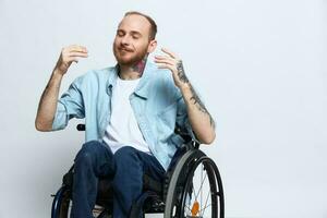 une homme dans une fauteuil roulant sourire, copie espace, avec tatouages sur le sien bras est assis sur une gris studio arrière-plan, le concept de santé est une la personne avec handicapées, une réel la personne photo