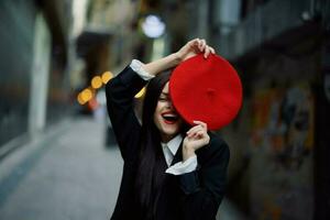 mode femme sourire avec les dents et amusement touristique dans élégant vêtements dans veste et rouge béret en marchant vers le bas étroit ville rue en volant cheveux, voyage, français style, cinématique couleur, rétro style. photo