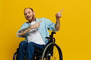 une homme dans une fauteuil roulant problèmes avec le musculo-squelettique système regards à le caméra spectacles une doigt sur, avec tatouages sur le sien mains est assis sur une Jaune studio arrière-plan, santé concept homme avec handicapées photo