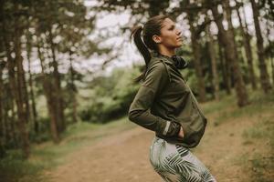 Jeune belle coureuse écoutant de la musique et prenant une pause après le jogging dans une forêt photo