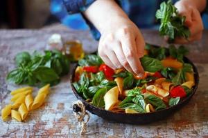 le chef mélange les pâtes avec le basilic et les épices dans une casserole photo