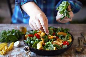 le chef mélange les pâtes avec le basilic et les épices dans une casserole photo