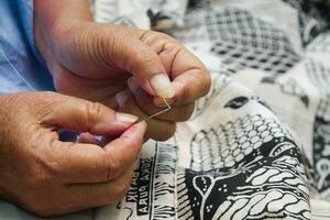 proche en haut photo de une femme mains couture batik tissu dans Indonésie