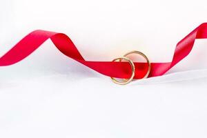 d'or mariage anneaux pour engagement. mariage d'or anneaux avec blanc, rose rubans Contexte. anneaux sur le blanc et rouge Rose. le mariage anneaux est le symbole de traditionnel mariage de paire les amoureux. photo