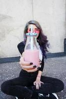 heureux bel adolescent avec des lunettes de soleil roses acclamations et apprécie une boisson rose assis sur le sol urbain photo