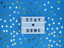 caisson lumineux avec citation de séjour à la maison sur fond bleu avec des confettis. quarantaine de noël. photo