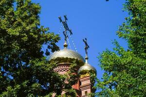 dôme de le orthodoxe église avec des croix, vue par le branches de des arbres contre le bleu ciel photo