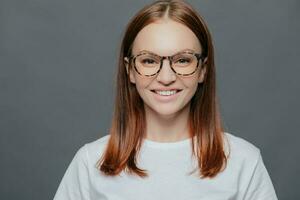 agréable Jeune femme, foncé cheveux, transparent lunettes. décontractée vêtements, en bonne santé peau. positif regarder, parfait dents. isolé sur gris. photo