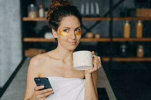 euro fille des textes avec café. femme s'applique œil patchs, se détend. hispanique fille dans serviette. soir corps se soucier. photo