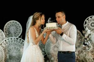 les jeunes mariés coupent et goûtent joyeusement le gâteau de mariage photo