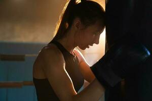 femmes soi la défense fille pouvoir. fort femme combattant repos après bats toi formation sur boxe anneau. fort fille fatigué après perforation boxe sac. formation journée dans salle de sport. force en forme corps faire des exercices entraînement. photo