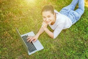 Jeune femme mensonge sur vert herbe pelouse dans ville parc travail sur portable PC ordinateur. free-lance affaires concept photo