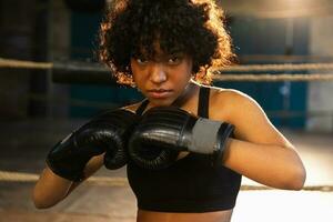 tollé indépendant fille pouvoir. en colère africain américain femme combattant avec boxe gants à la recherche sérieux agressif permanent sur boxe anneau. fort puissant combattant fille formation coups de poing. photo