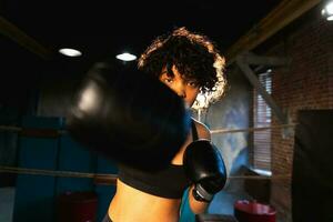 femmes soi la défense pouvoir. africain américain femme combattant perforation avec boxe gants à caméra. en bonne santé fort fille perforation formation poinçons à la recherche concentré droit. en forme corps entraînement. photo