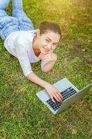 Jeune femme mensonge sur vert herbe pelouse dans ville parc travail sur portable PC ordinateur. free-lance affaires concept photo