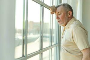 triste fatigué solitaire déçu plus âgée Sénior homme à Accueil seule. malheureux grand-père à la recherche Malheureusement à l'extérieur fenêtre expérience douleur relatif décès mal nouvelles. stressé aîné homme Souffrance de solitude. photo