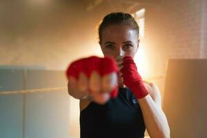 femmes soi la défense fille pouvoir. fort femme combattant perforation avec rouge boxe enveloppements des sports protecteur des pansements. fille perforation formation poinçons à la recherche concentré droit. en forme corps entraînement. photo