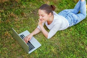 Jeune femme mensonge sur vert herbe pelouse dans ville parc travail sur portable PC ordinateur. free-lance affaires concept photo