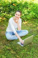 jeune femme assise sur une pelouse d'herbe verte dans le parc de la ville travaillant sur un ordinateur portable. concept d'entreprise indépendant photo