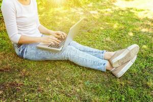 jambes de femme sur la pelouse d'herbe verte dans le parc de la ville, mains travaillant sur un ordinateur portable. concept d'entreprise indépendant photo