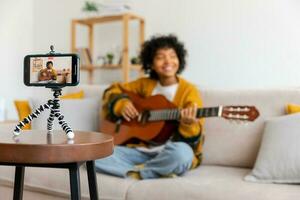 blogueur guitariste. africain américain fille blogueur en jouant guitare parlant à webcam enregistrement vlog. social médias influenceur femme diffusion à Accueil à l'intérieur. la musique contenu créateur diffuser Didacticiel. photo