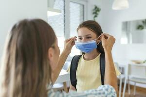 Jeune mère Aidez-moi sa fille portant médical masque à préparer aller à école. éviter covid-19 ou coronavirus épidémie. retour à école photo