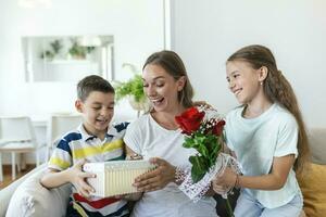 content les enfants donnant cadeau un fleurs à mère. content les mères journée les enfants garçon et fille féliciter souriant mère, donner sa fleurs bouquet de des roses et une cadeau boîte pendant vacances fête photo