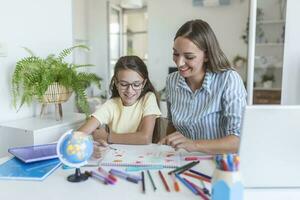 Jeune fille Faire sa école devoirs avec sa mère, à maison, elle est l'écriture sur une livre. mère et enfant fille Faire devoirs l'écriture et en train de lire à Accueil photo