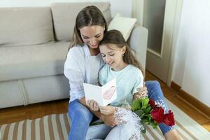 content de la mère journée. enfant fille félicite maman et donne sa carte postale et fleurs. maman et fille souriant et étreindre. famille vacances et unité. photo