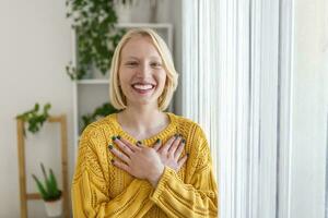 portrait de content millénaire femelle bénévole en portant plié mains sur poitrine, à la recherche à caméra. gentil souriant Jeune femme sentiment reconnaissant, montrant appréciation, Reconnaissance croyez charité concept. photo