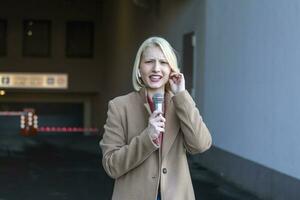 tondu portrait de professionnel femelle journaliste à travail. Jeune femme permanent sur le rue avec une microphone dans main et souriant à caméra. horizontal tir. sélectif concentrer sur femme photo