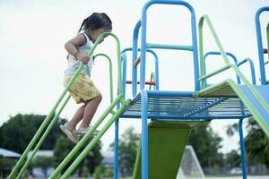 une fille est escalade en haut une acier échelle à une faire glisser dans une Cour de récréation. photo