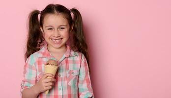 malicieux peu fille souriant à la recherche à caméra, en portant la glace crème dans gaufre cône, isolé sur rose Couleur Contexte photo