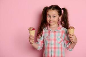 magnifique peu enfant fille sourit à la recherche à caméra, en portant deux gaufre cônes avec la glace crème, isolé sur rose Contexte photo