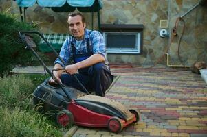 attrayant Masculin jardinier 40 ans, souriant à la recherche à caméra tandis que remplacer filtre sur électrique pelouse tondeuse dans le jardin photo