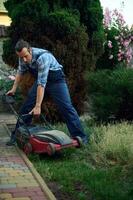 professionnel paysagiste en utilisant électrique pelouse tondeuse, Coupe herbe avec moderne jardinage équipement. aménagement paysager industrie photo