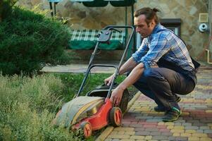 professionnel jardinier prend le Couper herbe en dehors de le filtre, recharge le électrique pelouse tondeuse dans le maison arrière-cour photo