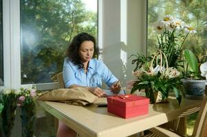 femelle fleuriste dessin sur presse-papiers une composition de fleurs pour spécial la vie événement, séance à table dans une fleur magasin photo