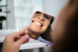 réflexion dans miroir de une femelle patient dans dentaire chaise, admiratif sa sourire et les dents après les dents blanchiment procédure photo