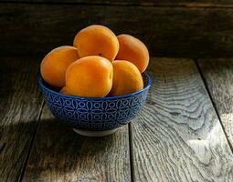 mûr Jaune abricots dans une bleu céramique bol sur une en bois tableau. photo