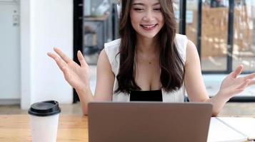 jeune femme d'affaires asiatique portant des écouteurs étudiant en ligne en regardant un podcast de webinaire sur un ordinateur portable, en écoutant et en apprenant la conférence téléphonique du cours d'éducation, en prenant des notes assis à un bureau, en concept d'apprentissage en ligne photo