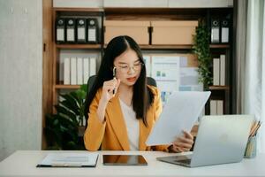 femme asiatique confiante avec un sourire debout tenant un bloc-notes et une tablette au bureau. photo